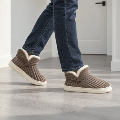 Man loopt in bruine warme winter pantoffels door de hal over een koele laminaatvloer